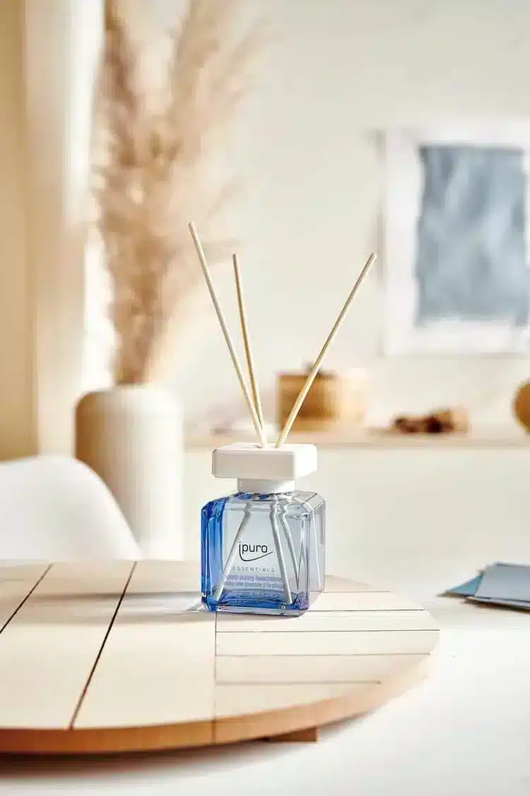 Ipuro Essentials Sunny Beachtime geurstokjes in blauwe fles op houten tafel met pluimgras